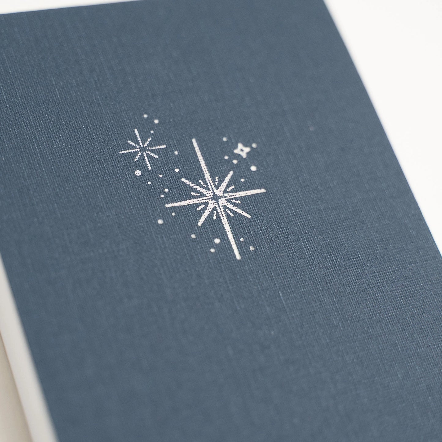 Small memo denim blue notebook with sparkle star design and Archer and Olive branding debossed in silver zoomed in at an angle.
