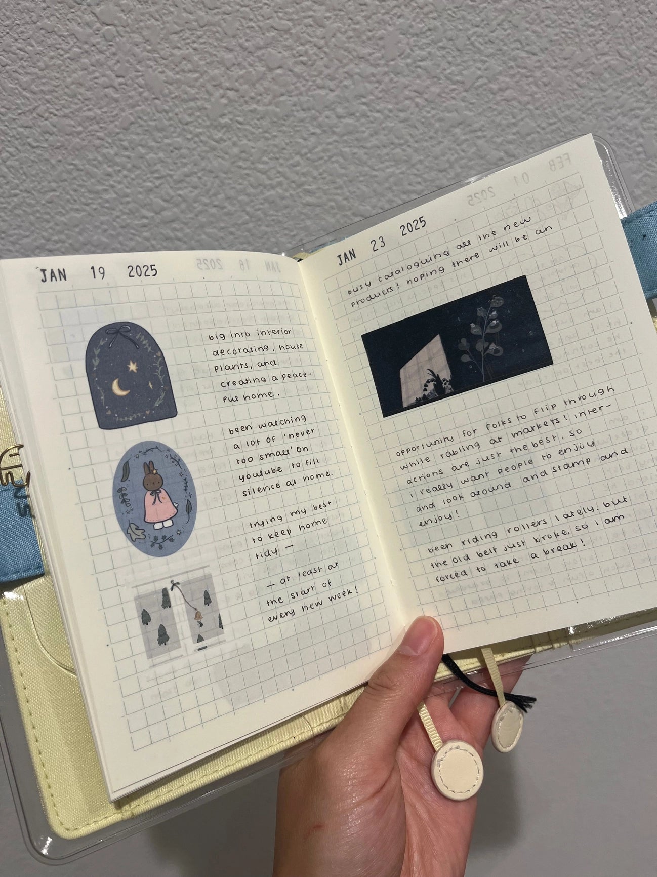 Open notebook with handwritten entries and stickers, held by a hand against a plain background. The page shows cute stickers of bunny and night time scene in a planner with tidy handwrittng.
