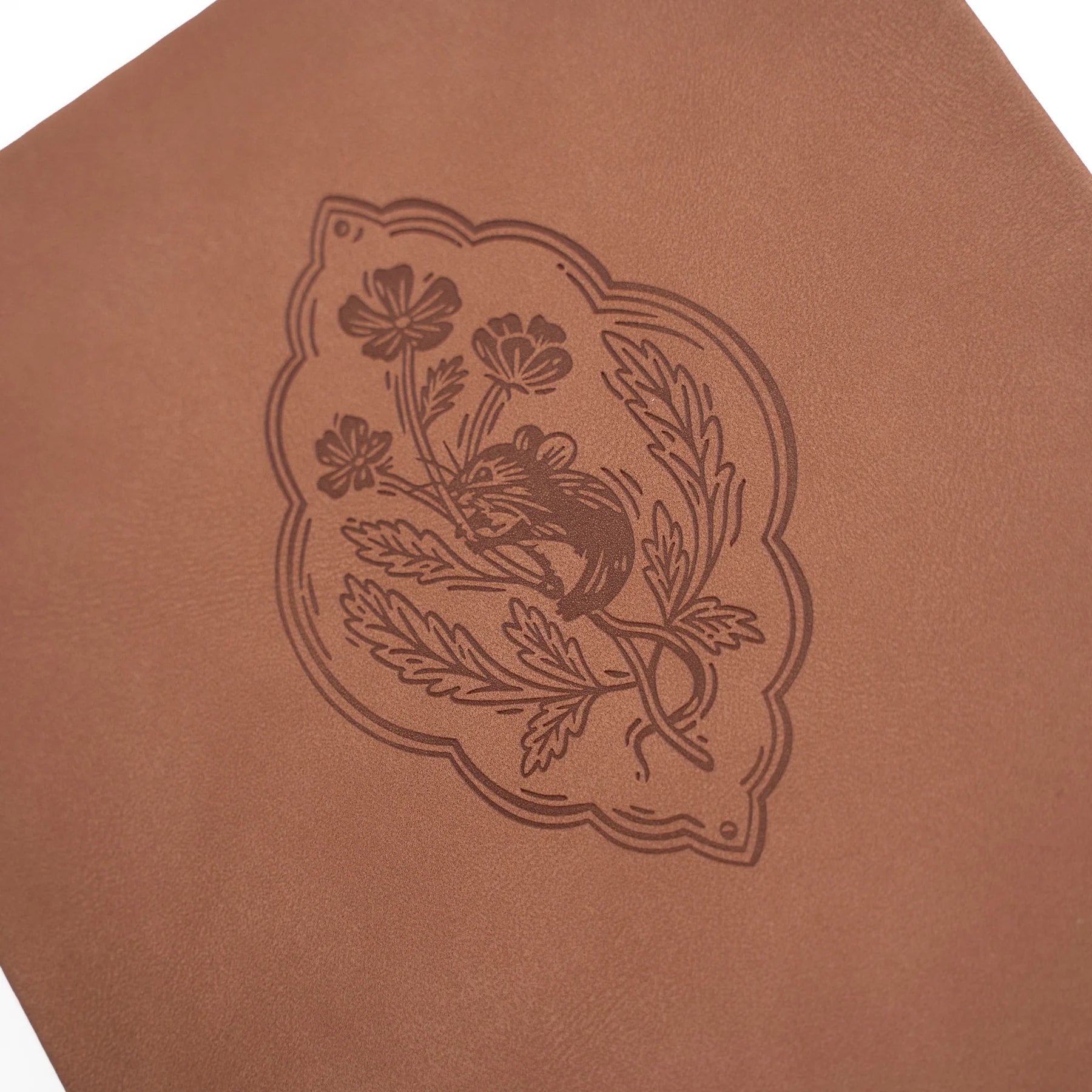 Zoomed in image of Archer and Olive's Field Mouse cover which is brown vegan leather notebook with a symbol of flowers and a little mouse climbing up the stalk.