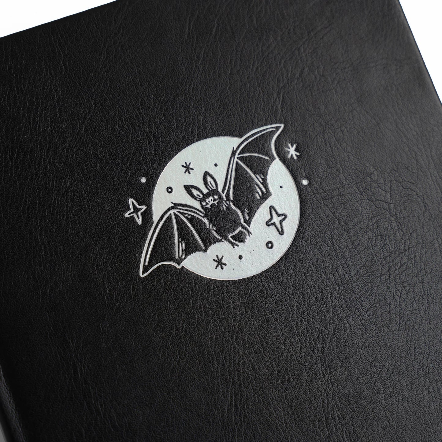 Archer and Olive Cute Bat - Cover Zoomed in, black leather surface with a bat illustration on a moon and star background