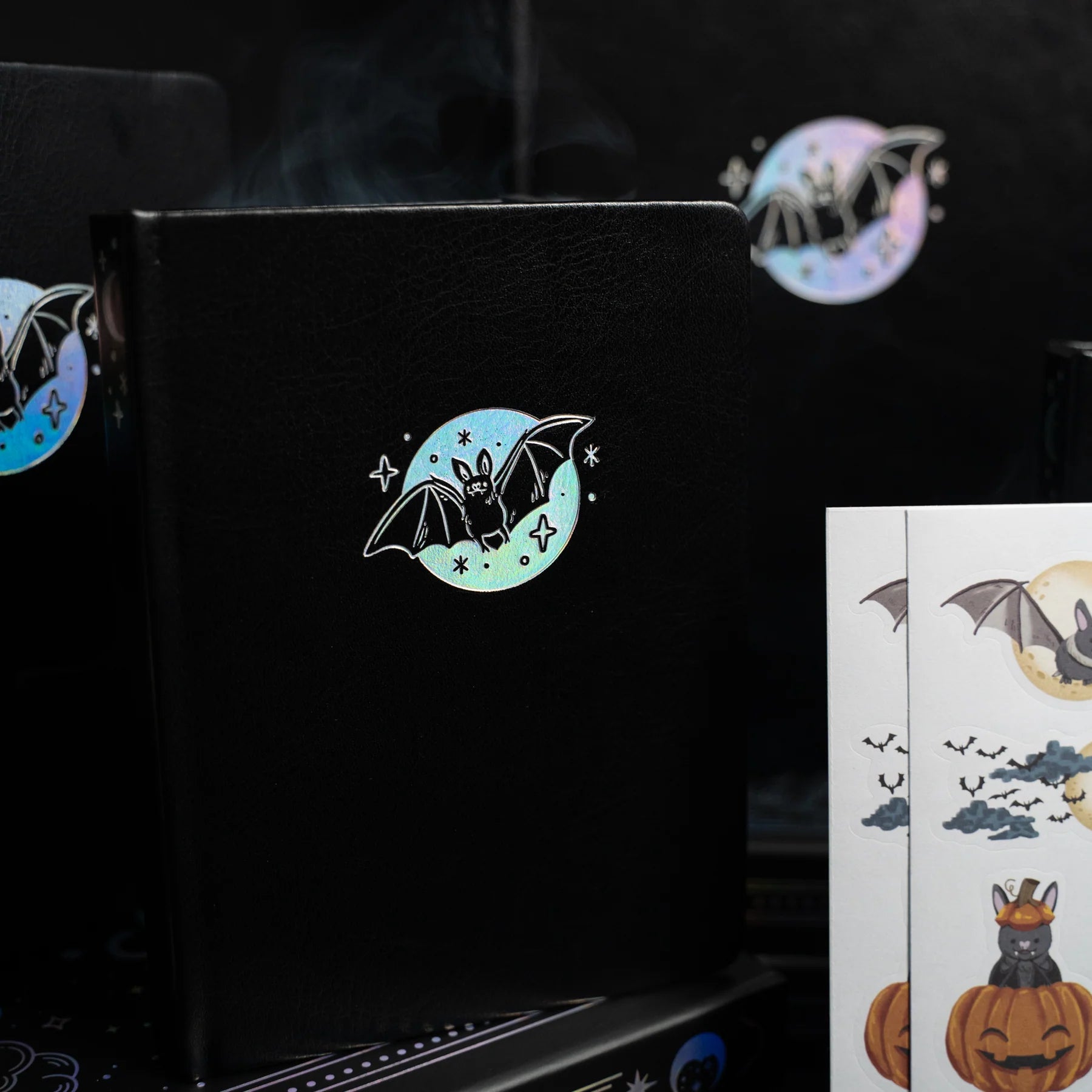 Archer and Olive Cute Bat - Black notebook with a bat illustration and additional stickers on a dark background