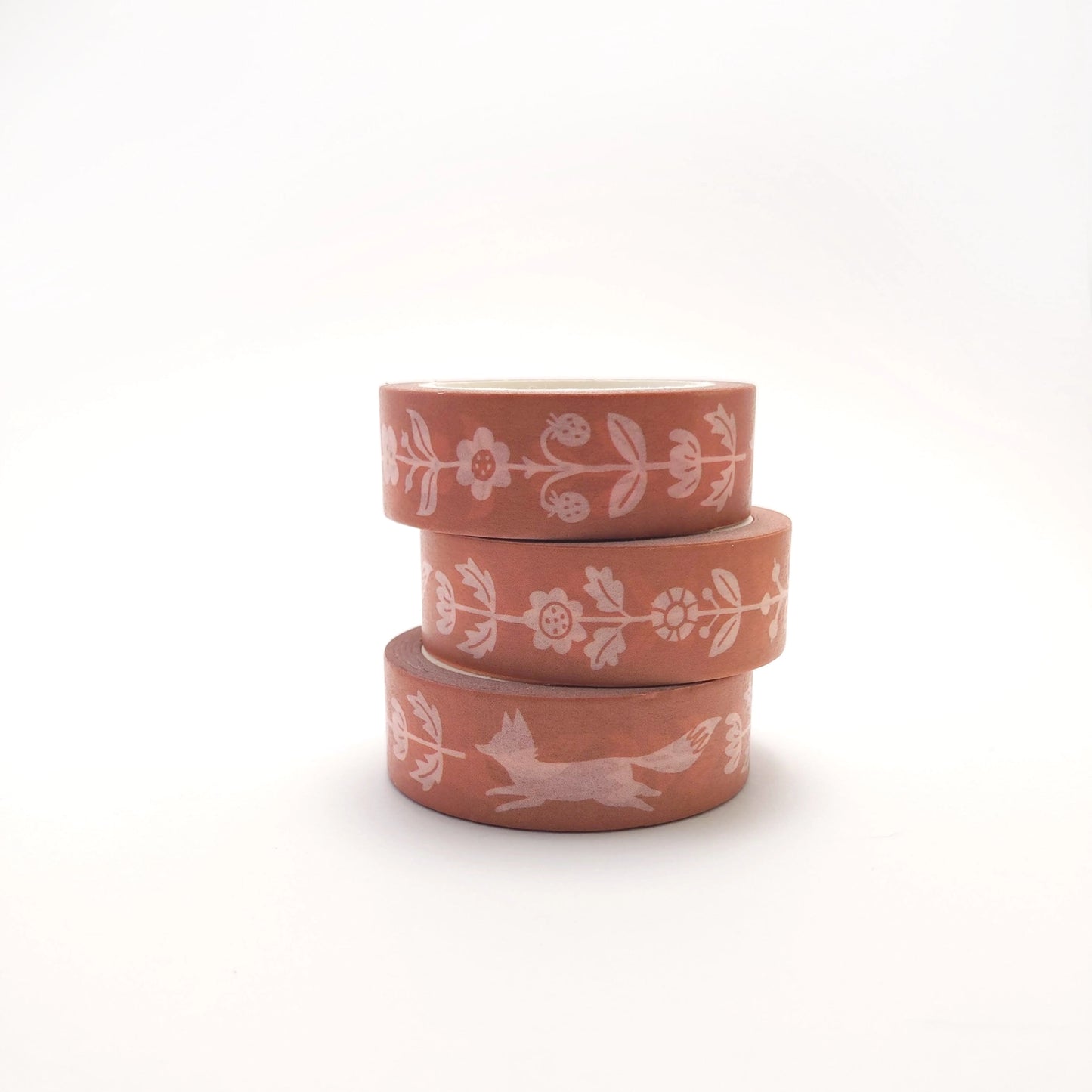 A roll of washi tape pink with white folk decorations of flowers and foxes.